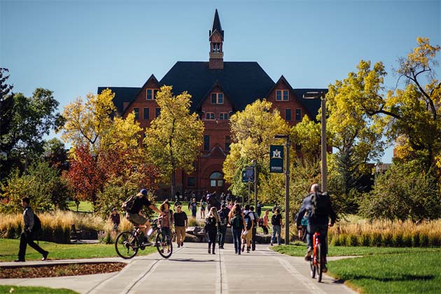 Fall campus scene with Montana Hall in the background and students walking or biking