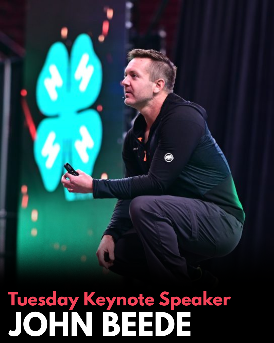 john beede kneeling on a stage with a 4-H clover in the background