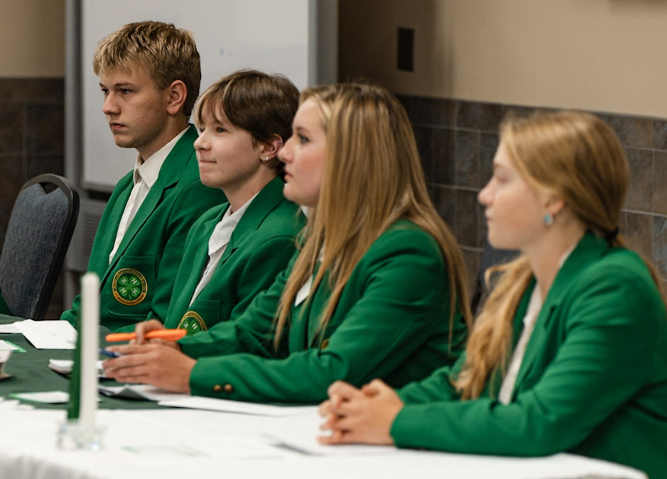 Four 4-H leaders sit at a table in green blazers, focused on the topic at hand.