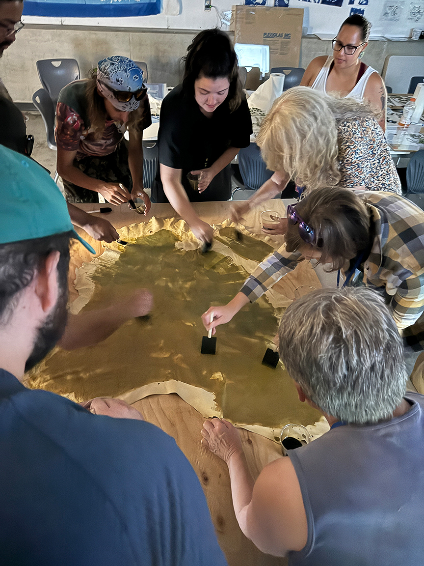 The workshop gathers around a deer hide, everyone helping to coat the material in cyanotype ink.